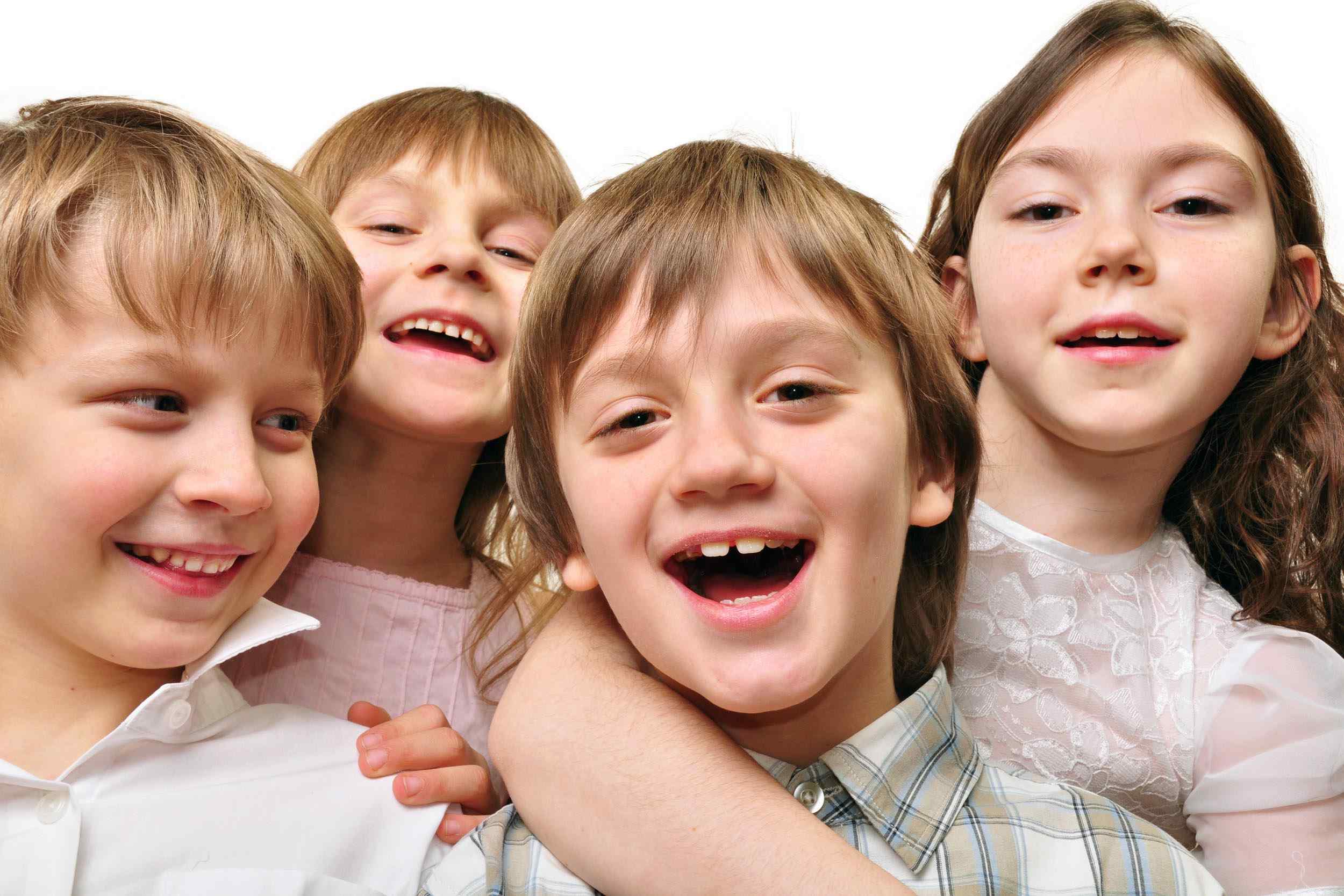 Vier lächelnde Kinder in hellen Hemden stehen dicht beieinander vor einem schlichten weißen Hintergrund und wirken glücklich und fröhlich.