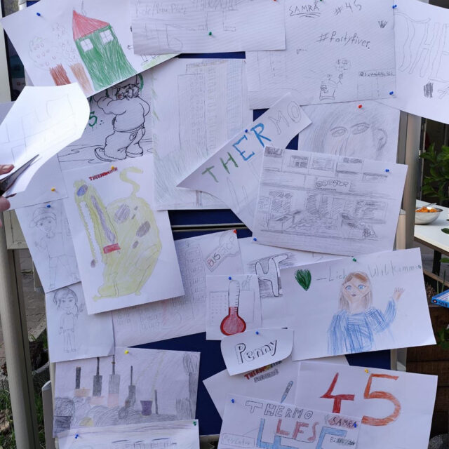 Eine Pinnwand mit verschiedenen handgezeichneten Skizzen und farbigen Zeichnungen, darunter Gebäude, Menschen, ein grünes Herz, Thermometer und die Zahl 45, die alle in einer collageartigen Darstellung angeheftet oder aufgeklebt sind.